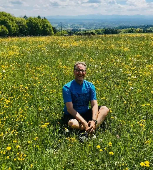 Sebastian Morgner sitzt in einer Blumenwiese über dem Ammersee