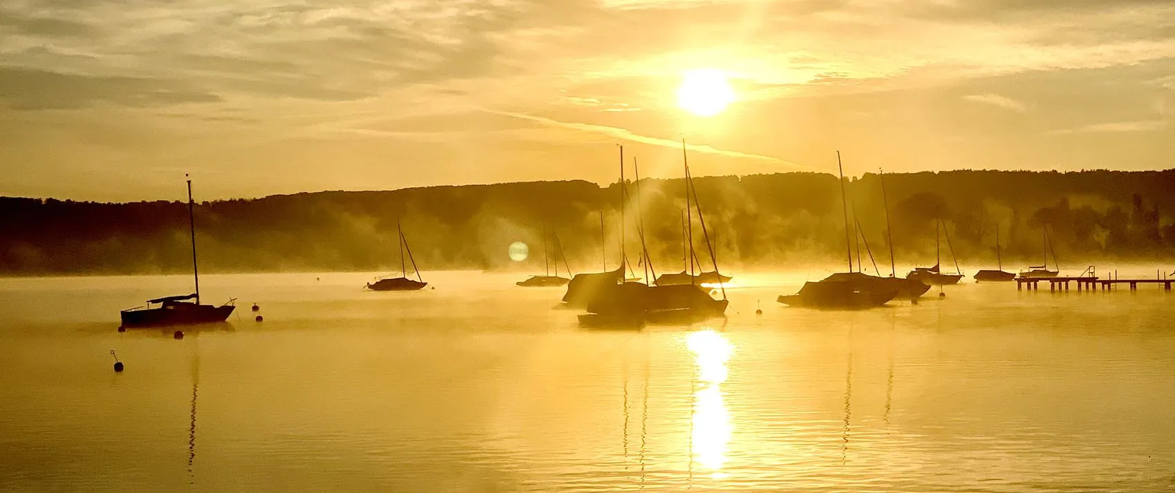 Segelboote im Morgennebel auf dem Ammersee, dahinter die aufgehende Sonne